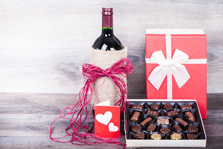 Red wine bottle, box of chocolates, love message and gift with decoration by red heart on wooden table. Valentines day celebration concept. Copy space.の写真素材
