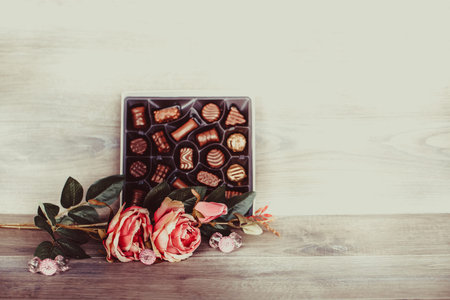 Box of chocolates and roses on wooden table. Valentines day celebration concept. Copy space.