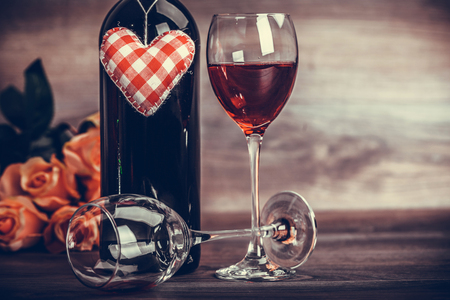Red wine bottle, two glasses of wine, rose with decoration by red hearts on wooden table. Valentines day celebration concept. Copy space.Close up.の写真素材