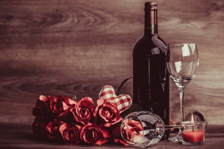 Red wine bottle, two glasses of wine, roses with decoration by red heart on wooden table. Valentines day celebration concept. Copy space.の写真素材