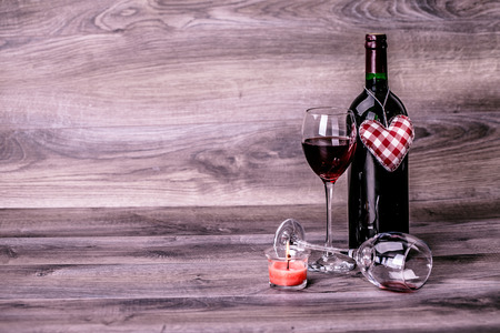 Red wine bottle, two glasses of wine, rose with decoration by red hearts on wooden table. Valentines day celebration concept. Copy space.の写真素材