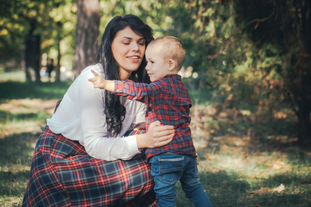 Smiling mother and little son playing together in a park. Mum hugging shy baby. Sunny  autumn day. Close up. Copy-space. Outdoor shot.Happy familyの写真素材