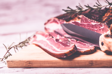 Smoked very delicious bacon with rosemary and knife on a wooden rustic background. Top view.Copy pasteの写真素材