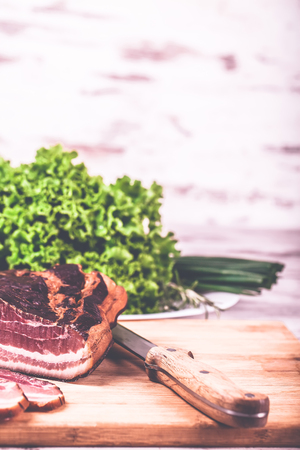 Smoked very delicious bacon with lettuce and knife on a wooden rustic background. Top view.Copy pasteの写真素材
