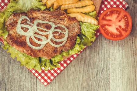 Tasty pork meat roast on the grill with fries, fresh lettuce and tomato on a wooden background. With empty space for your text. View from above.の写真素材