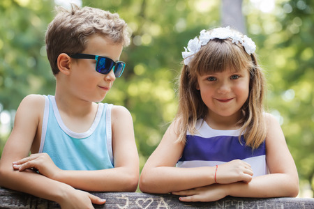 First love. Little sweet boy and happy smiling girl standing by the bench in the park and having fun.の写真素材