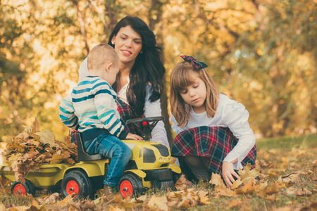 Smiling mother, doughter and little son playing together in a park in autumn. They are having a good time while playing with the dry fallen leaves.Happy familyの写真素材