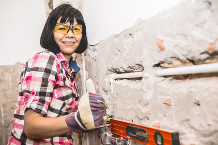Clever woman repairing her bathroom sink pipe with positive attitude. Woman using Bubble Spirit Water Ruler Tool  and checking the tubes in the bathroom.の写真素材