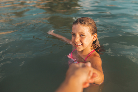 Follow me concept. Cute little girl pulling mom's hand - hand in hand walking through the waterの写真素材