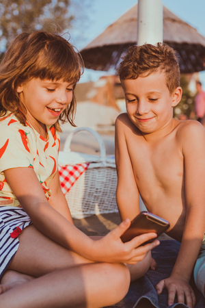 Portrait of positive happy children playing with mobile phones on sandy beach togetherの写真素材