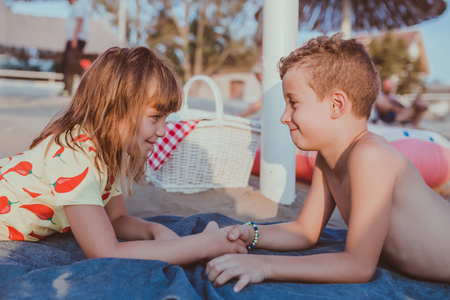 Side view of a little boy and a girl while lying on the beach and holding hands. Friendship, happy couple, first loveの写真素材