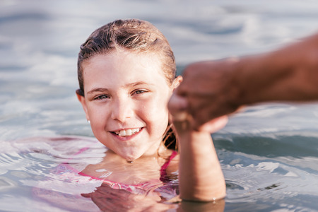 Follow me concept. Cute little girl pulling mom's hand - hand in hand walking through the waterの写真素材