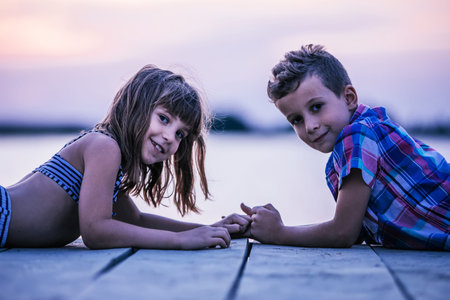 View from above of a little boy and a girl while lying on the wooden pier and holding hands. Happy...