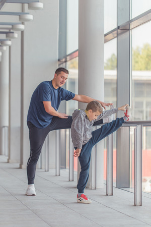 Little boy and his trainer doing stretching legs exercises together at a sports center. Father and son spend time together and lead a healthy lifestyle.Working Out Together. Fitness Day.の写真素材