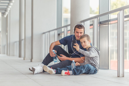 Little boy and his father taking a break and listening to the music together in a sports center. Father and son spend time together and lead a healthy lifestyle.  Making selfie photoの写真素材