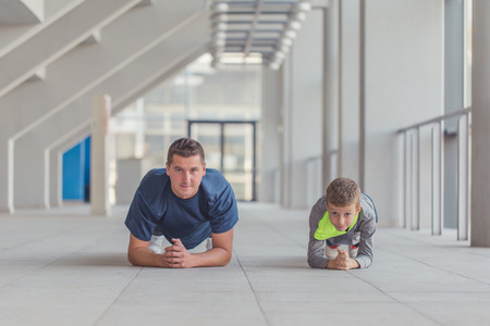 Little boy and his trainer doing push ups exercises together at a sports center. Father and son spend time together and lead a healthy lifestyle.の写真素材
