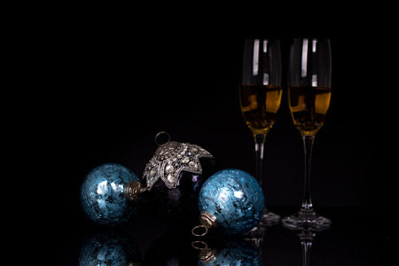 Two wine glasses with champagne, clock and Christmas ornaments on a black background with reflection. Copy space. Merry Christmas and Happy New Year, backgroundの写真素材