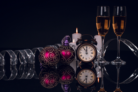 Two wine glasses with champagne, clock and Christmas ornaments on a black background with reflection. Copy space. Merry Christmas and Happy New Year, backgroundの写真素材