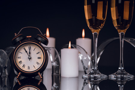 Two wine glasses with champagne, clock and candles on a black background with reflection. Copy space. Merry Christmas and Happy New Year, backgroundの写真素材