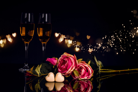 Two glasses of champagne, roses and two heart shape chocolates on black background with lights in the background. Love, Valentines day conceptの写真素材
