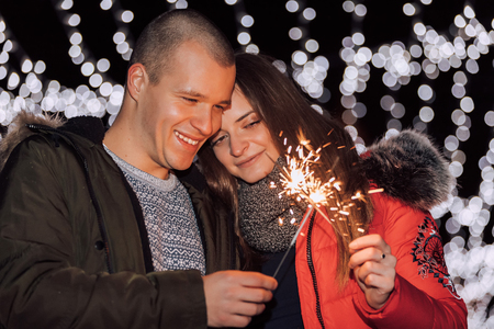 Young happy couple having fun with sparklers in winter city night.  The young man hugging his girlfriendの写真素材