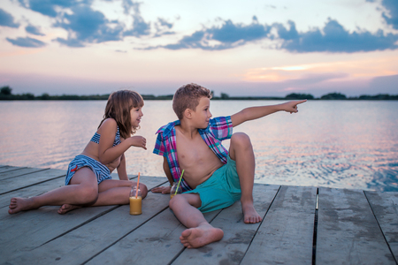Happy and positive children sitting by the river and having fun at sunsetの写真素材