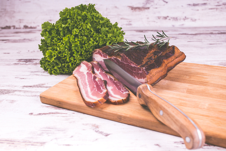 Smoked bacon with rosemary, lettuce and knife on wooden table - Image. Copy pasteの写真素材