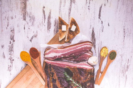 Smoked bacon with rosemary and spices in spoons on a wooden rustic background. Top view.Copy paste