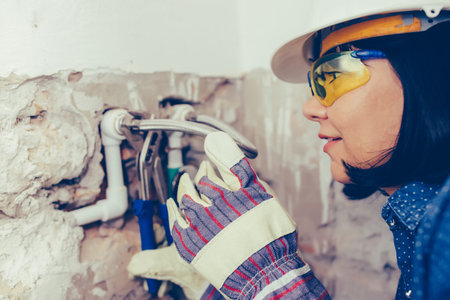Close up female plumber in gloves with wrenches repairs the pipes in the bathroom. Repair of pipes, valves, water meters.の写真素材