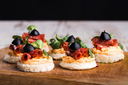 Delicious canapes with salami, olives and spices on a wooden backgroundの写真素材