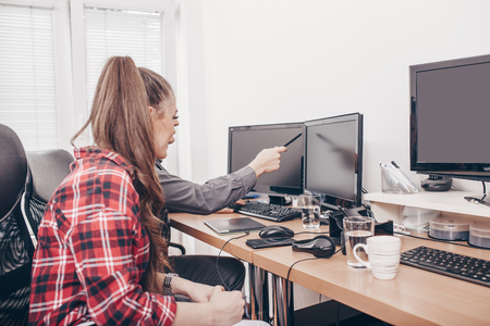 Image of happy young colleagues sitting in office, working on projekt and using desktop computersの写真素材