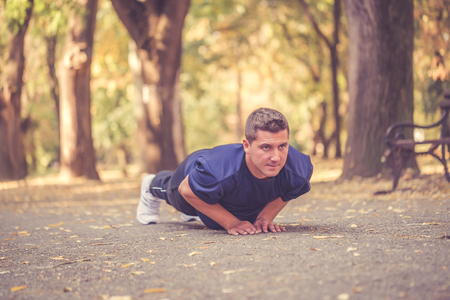 Picture of a young athletic man doing push ups in the park, preparing for morning workout.の写真素材