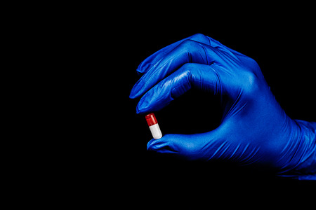 Doctor in sterile gloves, holding a medicine capsule on black background  - Imageの写真素材