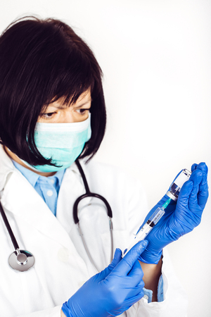 Female doctor in white lab coat and medical mask on white background holds insulin syringe and medicine in ampoule - Imageの写真素材