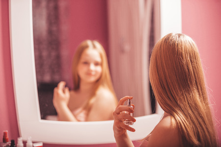 Teenage girl in a dress looking in the mirror and  applying perfume, at home - Imageの写真素材