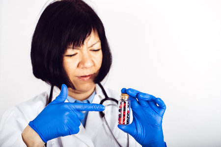 Female doctor in white lab coat and medical gloves holding glass bottle with black-red capsules. - Imageの写真素材
