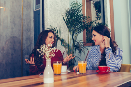 Happy female friends talking and drinking coffee while looking each other sitting in the table in a cafe. - Imageの写真素材