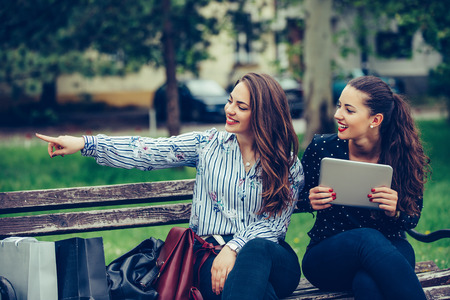 Two beautiful female friends holding a digital tablet pointing away in the street - Imageの写真素材