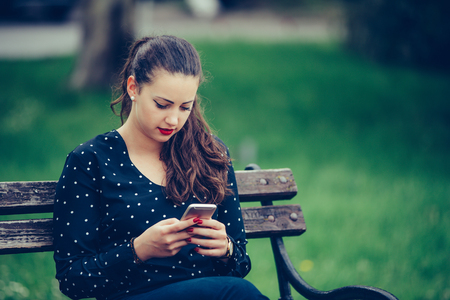 Girl texting on the smartphone sitting in a bench in a park - Imageの写真素材