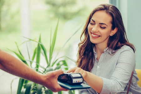 Young woman paying by credit card at cafe. Woman entering security pin in credit card reader with...