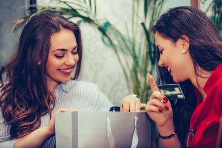 Two young women sharing their new purchases with each other. They having coffee break after shopping. Consumerism, shopping, lifestyle conceptの写真素材