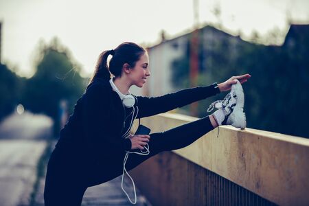 Beautiful girl is doing stretching exercise on the bridge, preparing for evening workoutの写真素材