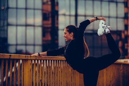 Young beautiful woman warming up on river bridge, preparing for evening workoutの写真素材