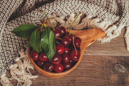 Fresh sour cherries with green leaves in wooden bowl on rustic brown background. Top viewの写真素材