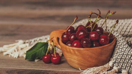 Fresh cherries with green leaves in wooden bowl on rustic brown backgroundの写真素材