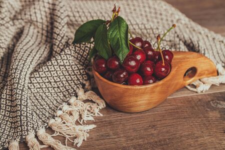 Fresh cherries with green leaves in wooden bowl on rustic brown backgroundの写真素材