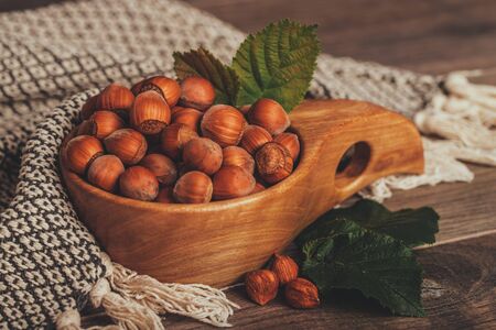 Hazelnuts with green leaves in wooden bowl on rustic brown background.の写真素材