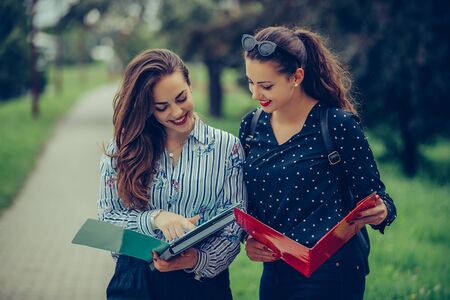 Two female friends, students learning reading a notebook and commenting in the streetの写真素材