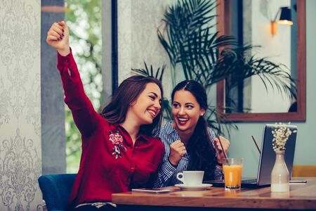 Two excited female friends celebrating success reading good news in a laptop at cafe.の写真素材