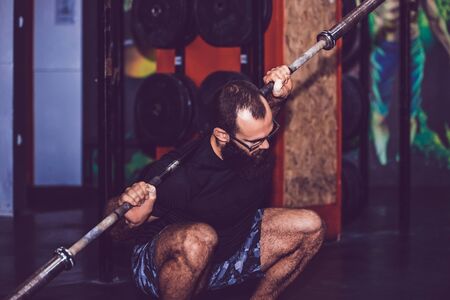 Young bearded man doing warm up exercises with weights in the gymの写真素材
